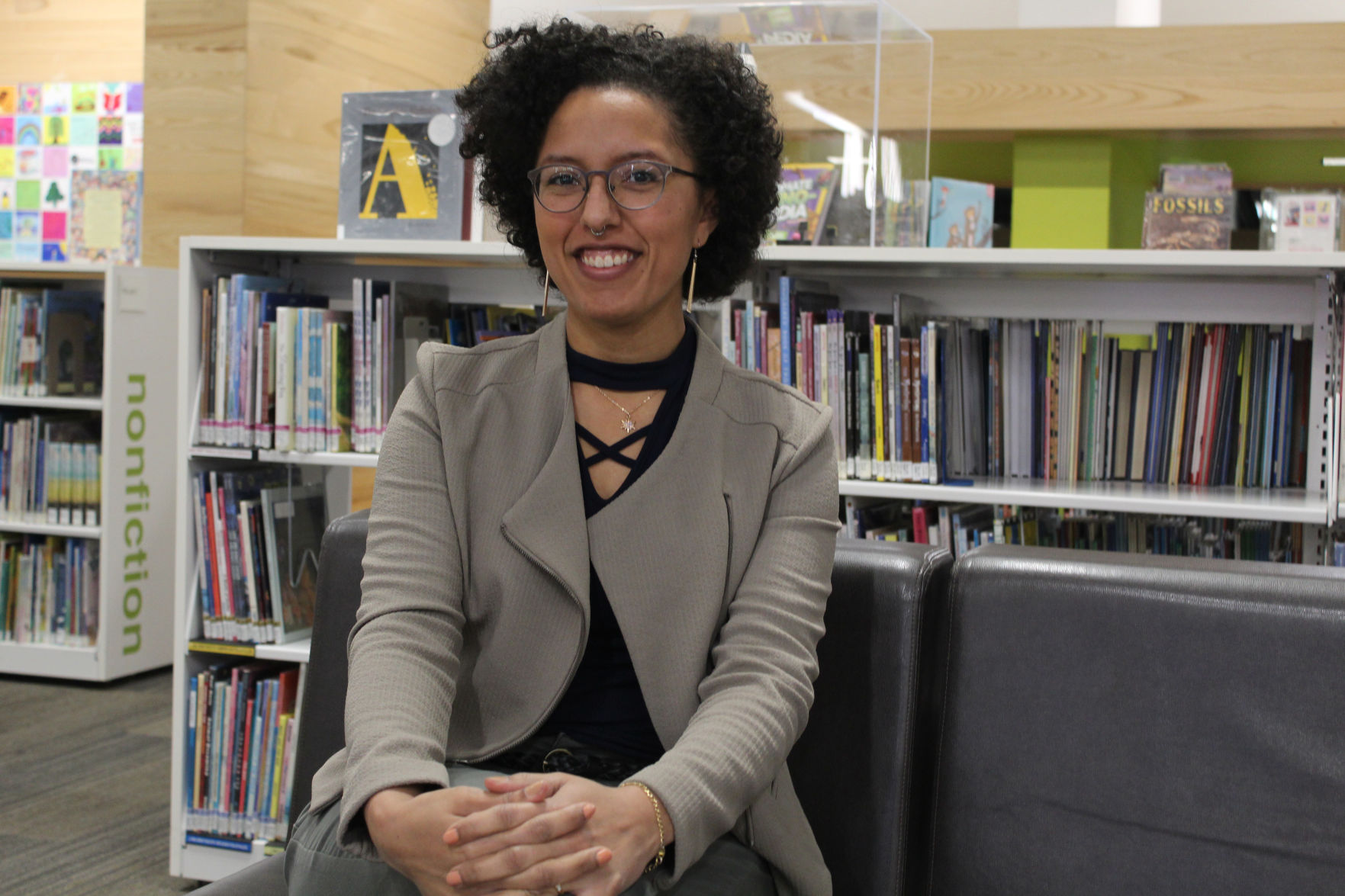 Alex Kimball-Williams sits and smiles as she poses for a photo in front of a wall of bookshelves